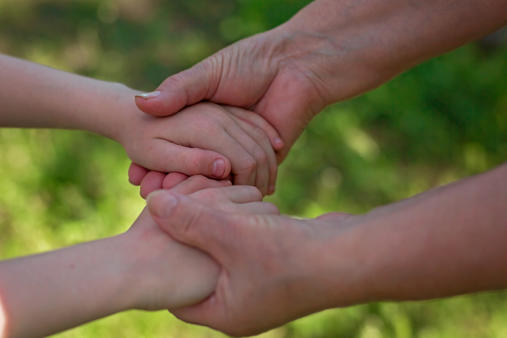 The hands of an adult hold the hands of a child.