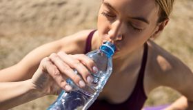 Sporty young woman drinking water outdoors after training