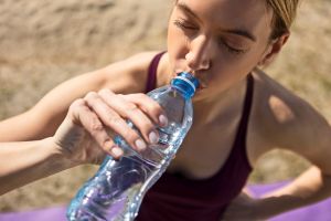 Sporty young woman drinking water outdoors after training