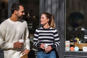 Man and woman holding takeaway cups outside a cafe talking