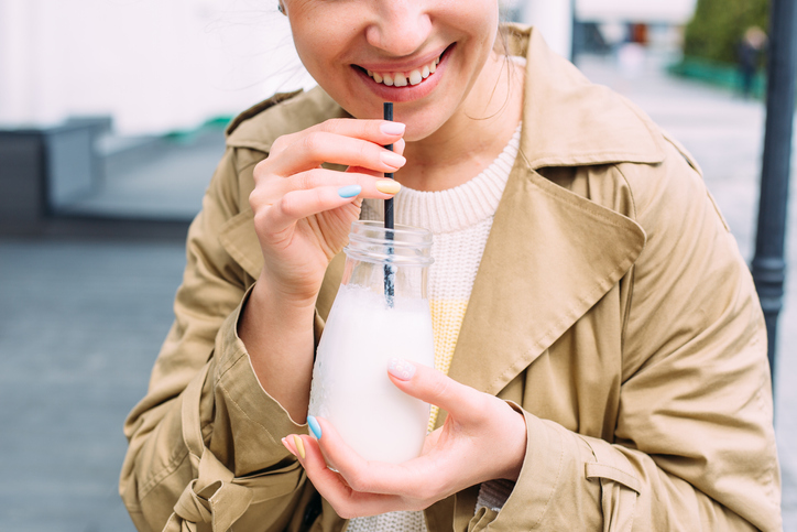 A Young Woman Drinks A Milkshake Outdoors From A Stylish Glass Jar With A Straw