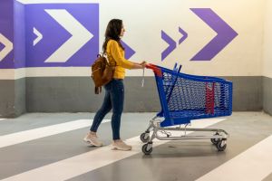 Young woman pushing an empty shopping cart in the supermarket garage.