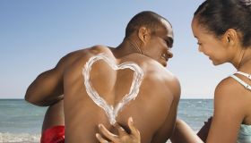 Hispanic woman drawing heart in sunscreen on boyfriend's back