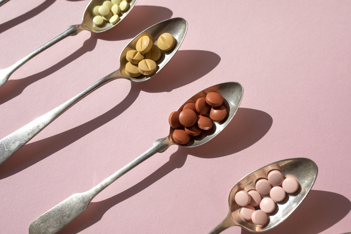 Various of spoons with pills and tablets on the pink background