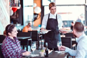 Smiling Waitress Bringing Dinner To Happy Couple