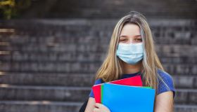 Student girl holding books while walking in school. She wears a mask for COVID-19, Coronavirus protection. Back to school concept