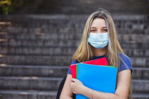 Student girl holding books while walking in school. She wears a mask for COVID-19, Coronavirus protection. Back to school concept