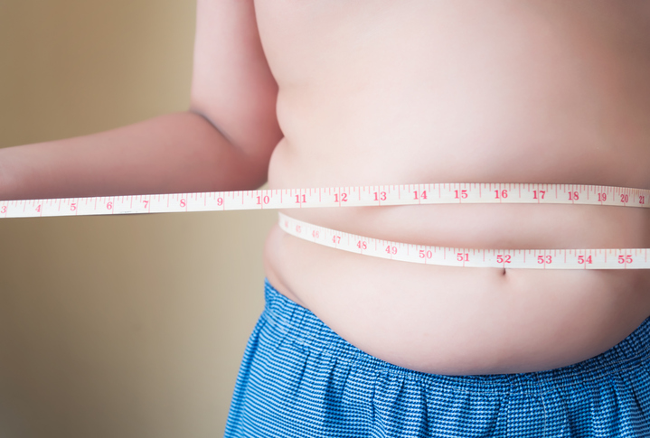 Midsection Of Overweight Boy Measuring Waist With Tape While Standing Against Wall