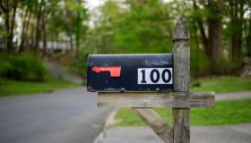 Black mailbox with number 100 on white fixed on wooden stand at road on American countryside.
