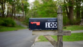 Black mailbox with number 100 on white fixed on wooden stand at road on American countryside.