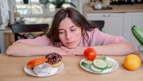 Young woman chooses between sweet donuts and fresh vegetables, healthy eating