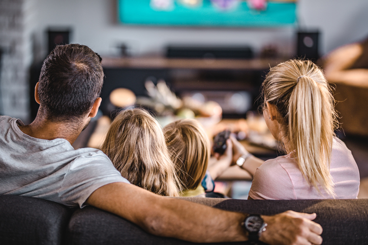 Rear view of a family watching TV on sofa at home.