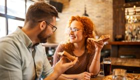 Couple talking while eating pizza and drinking beer in a pub