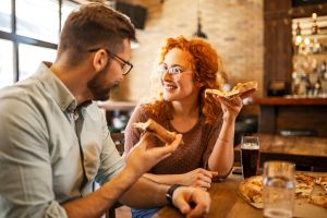 Couple talking while eating pizza and drinking beer in a pub