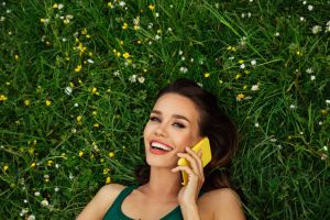 Smiling young woman lying on grass and using smartphone