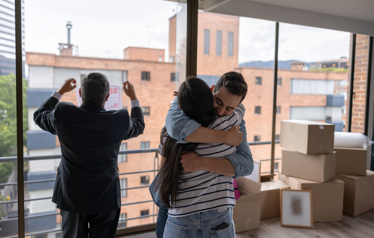 Couple moving house and hugging while the realtor removes the for sale sign