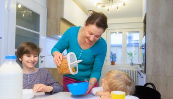 Happy mother pouring breakfast cereal in bowls for her sons at home