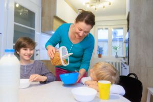 Happy mother pouring breakfast cereal in bowls for her sons at home