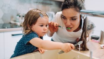 Mother and daughter brushing teeth together.