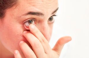 Close-up of a brown-eyed woman putting on corrective lenses in front of a mirror, white background.