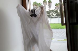 A funny little cute girl wearing a ghost costume having fun and dancing in Halloween's season. She's standing in front of the main door asking for candies in a Halloween afternoon day.