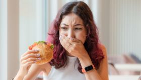 A girl eats a burger in a fast food cafe and feels nausea and heartburn. The concept of unhealthy food and food poisoning