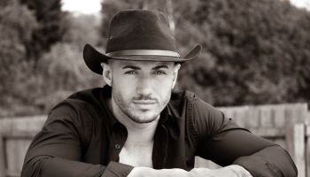 Sexy, handsome, hunky cowboy with hat open shirt and pecs looks at camera