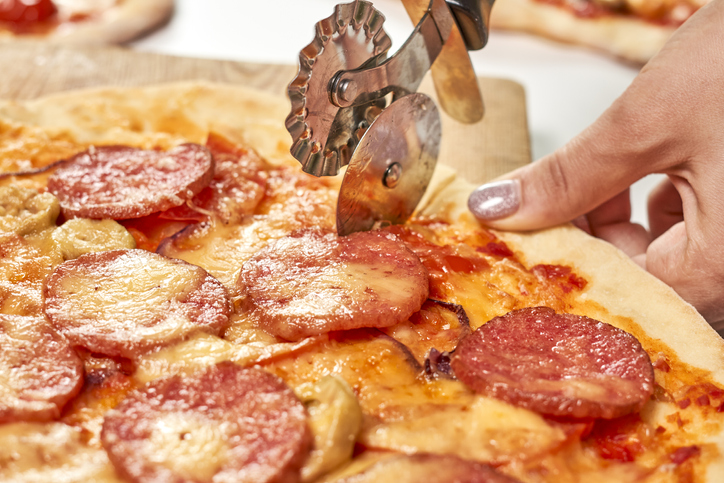 Closeup of a person cutting pizza into slices