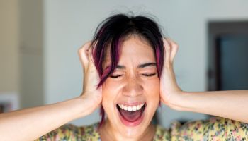 Young woman with head in hands screaming at home