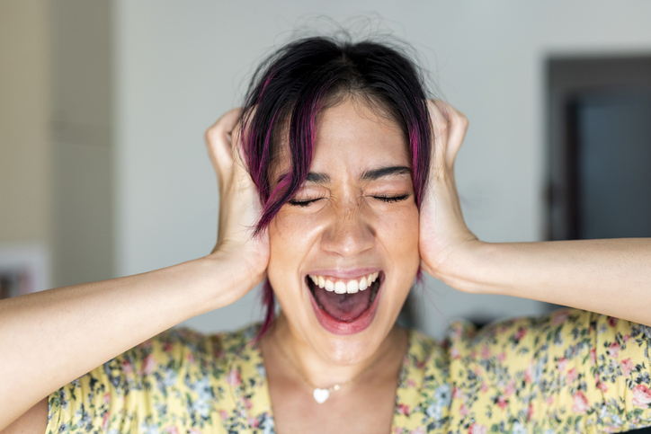 Young woman with head in hands screaming at home