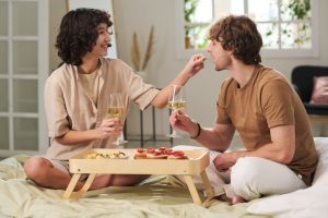 Happy young woman putting piece of snack in mouth of her husband