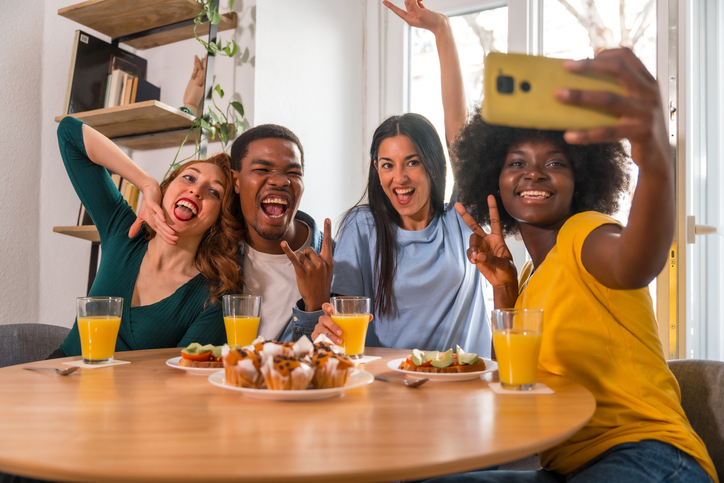 Multiethnic friends at a breakfast with orange juice and muffins at home, taking a selfie