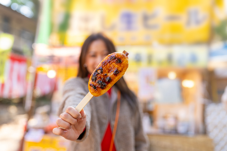 Asian woman holding grilled mochi with soy sauce on sticks at street market in Tokyo city, Japan.