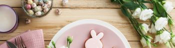 Easter brunch table setting. Spring Easter holiday concept with white, pink plate and napkin with decorative symbols holiday rabbit, eggs and bouquet of flowers on old wooden background. Top view.