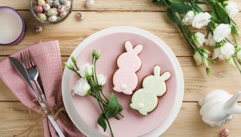 Easter brunch table setting. Spring Easter holiday concept with white, pink plate and napkin with decorative symbols holiday rabbit, eggs and bouquet of flowers on old wooden background. Top view.