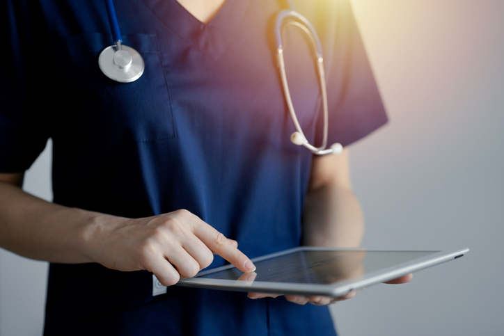 Doctor woman using tablet computer while standing near panorama window in clinic, close up. Physician or surgeon at work. Medicine concept