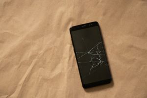 black phone with a cracked screen on a brown background close-up