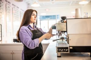 Female barista using espresso machine in modern coffeeshop