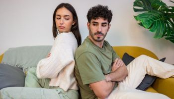 Young couple sitting on a sofa with their backs to each other.