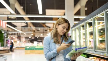 Young woman checking shopping list on smart phone in supermarket