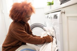 Smiling young woman loading clothes into a washing machine