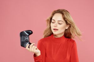 Woman with gamepad in hand entertainment video games lifestyle technology red blouse pink background