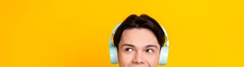Photo of nice student dressed striped t-shirt listen music in headphones look at promo empty space isolated on yellow color background