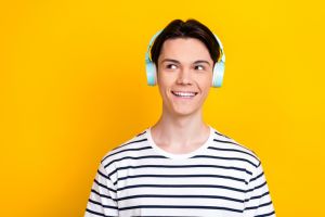 Photo of nice student dressed striped t-shirt listen music in headphones look at promo empty space isolated on yellow color background