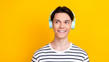 Photo of nice student dressed striped t-shirt listen music in headphones look at promo empty space isolated on yellow color background