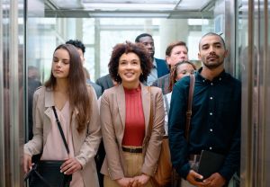 People, elevator and woman happy for job in business, internship and working in corporate career. Employees, serious expression and female person with smile for professional opportunity in office