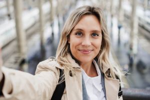 Smiling woman with highlighted hair taking selfie at train station