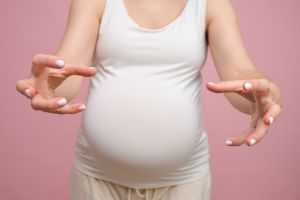 Pregnant woman angrily reaches her hands forward, studio pink background