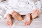 Feet of a couple in bed under the white blanket.