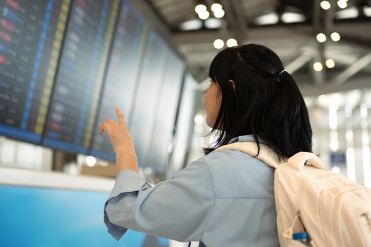 Young woman with a backpack checking flight departure board in the airport